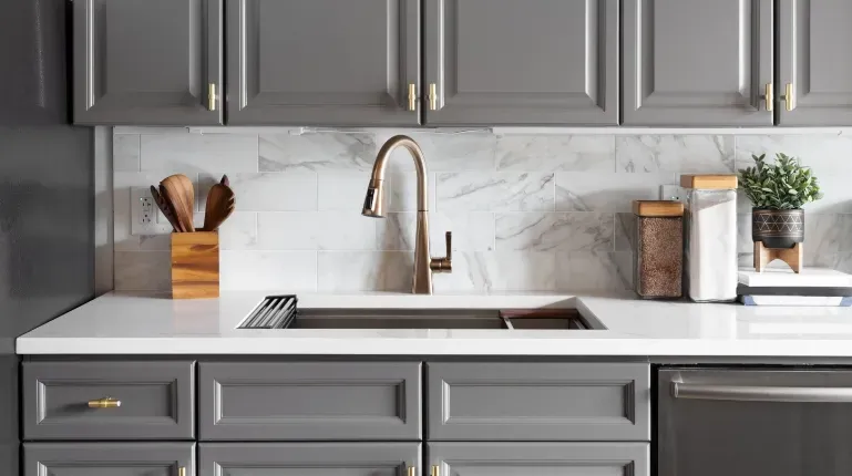 grey kitchen cabinets with marble walls and sink in center